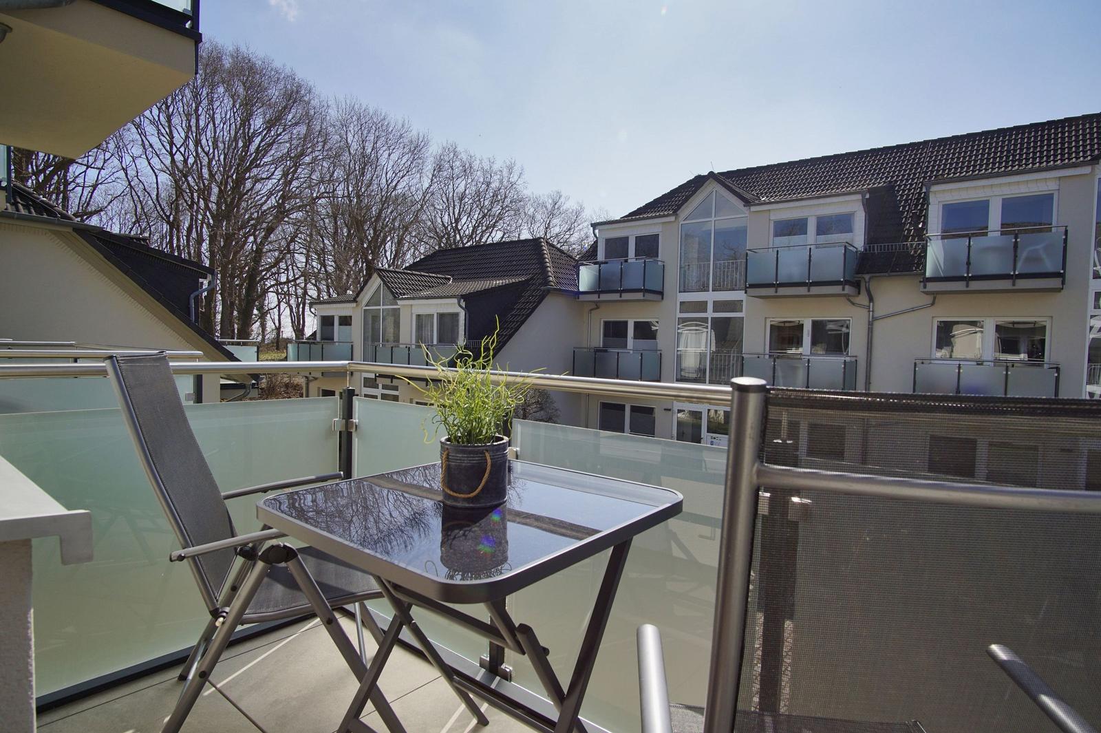 Terrasse mit Tisch, Stühlen und Pflanze. Blick auf moderne Wohnhäuser und Bäume.