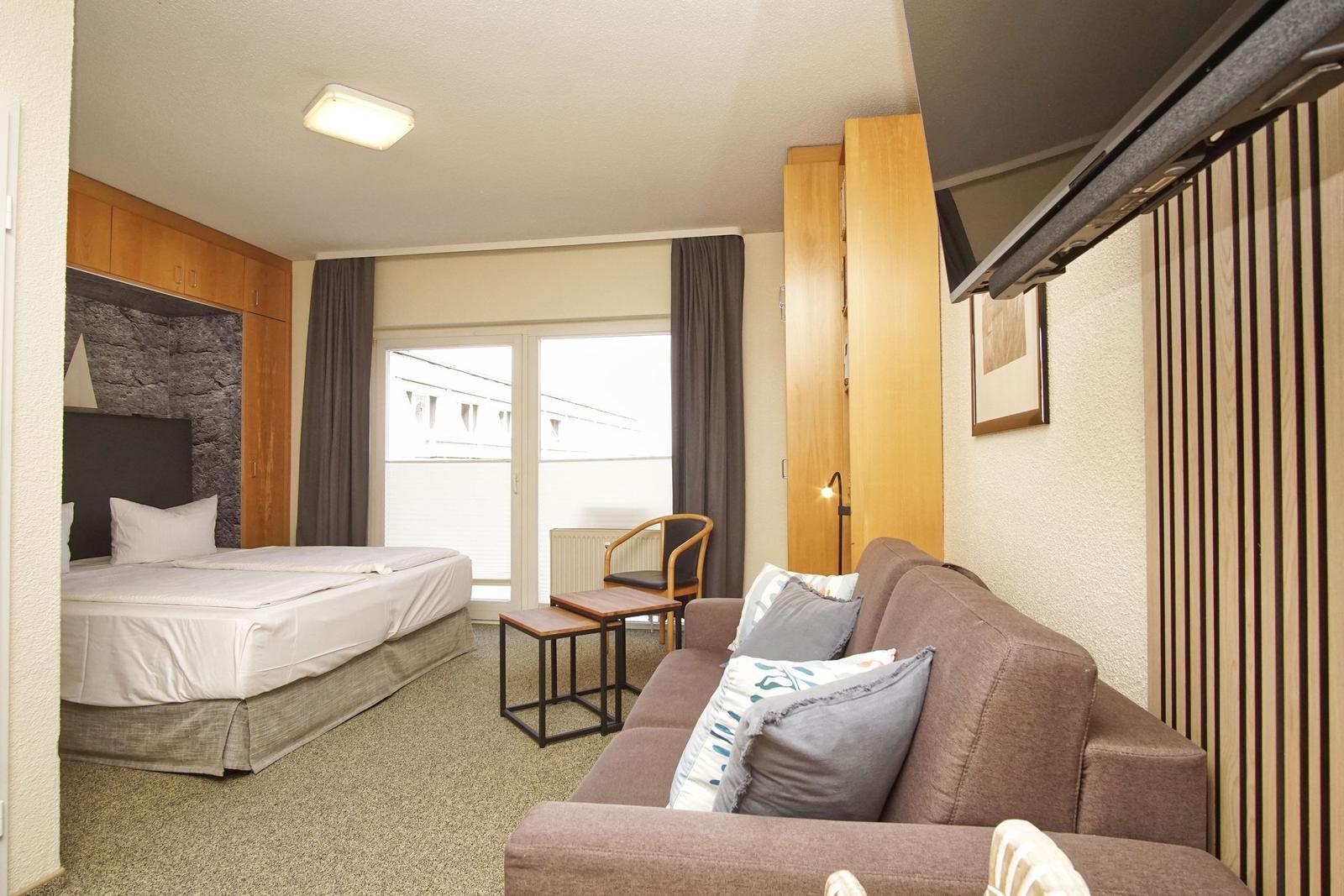 Schlafzimmer mit Bett, Sofa und Balkon. Holzmöbel und Steinwand sichtbar.