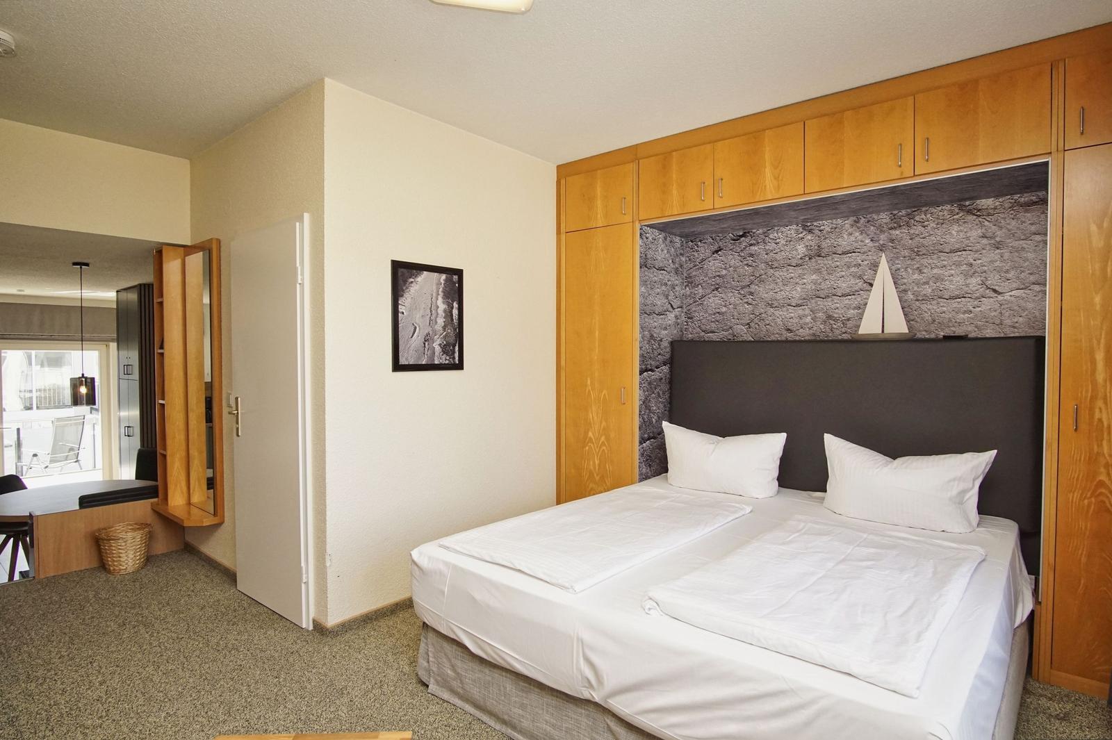 Schlafzimmer mit Doppelbett, Holzmöbel und Steinwand im Hintergrund.