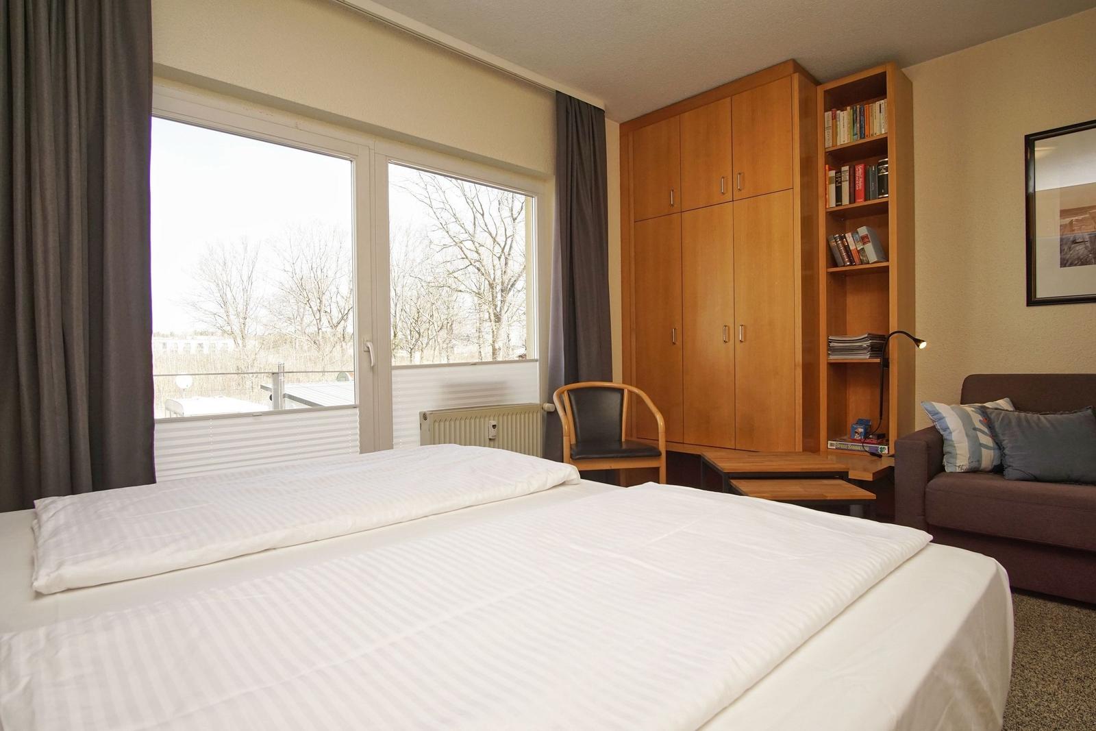 Ein Schlafzimmer mit Doppelbett, Bücherregal und Fenster mit Blick auf Bäume.