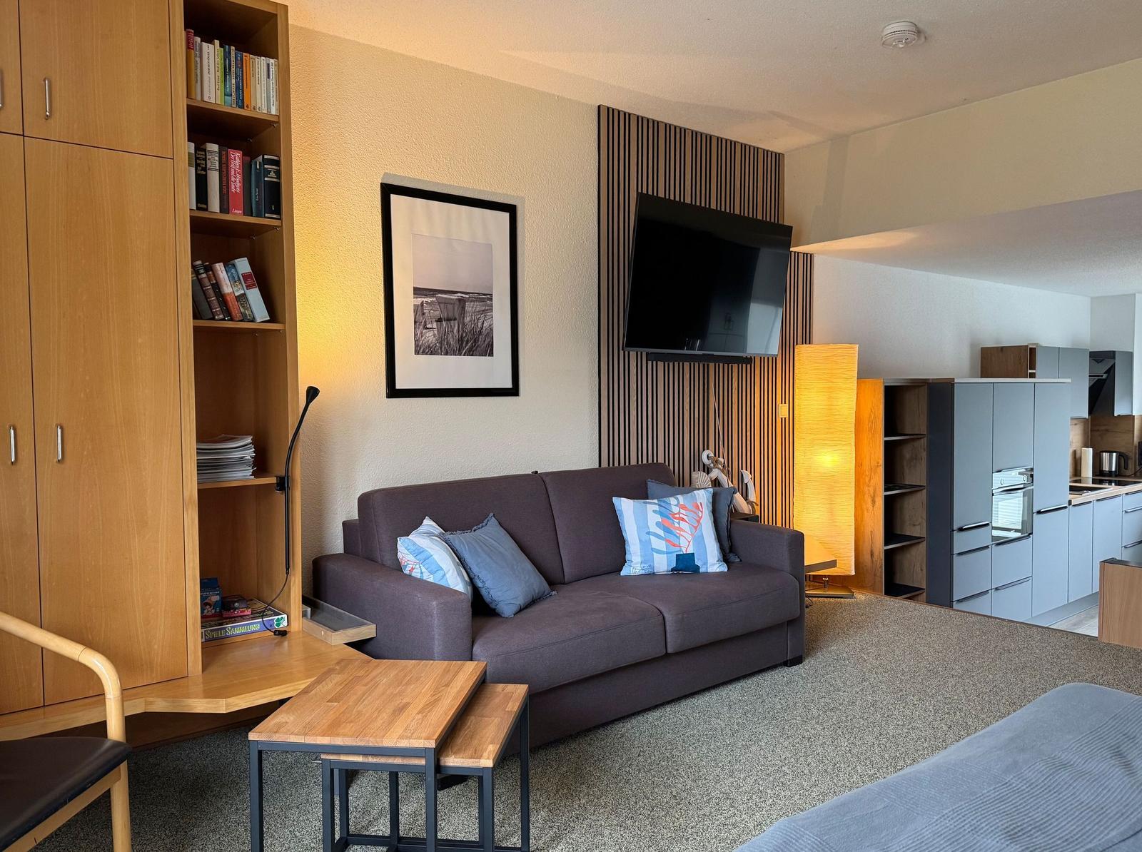 Wohnzimmer mit Sofa, Fernseher und Küchenbereich im Hintergrund.