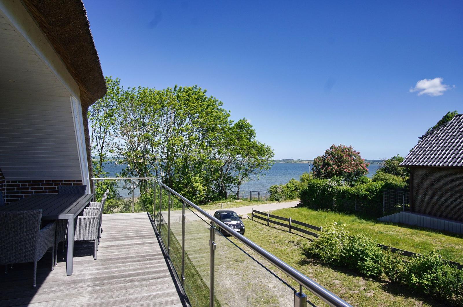 Terrasse mit Tisch und Stühlen, Blick auf Wasser und Bäume.