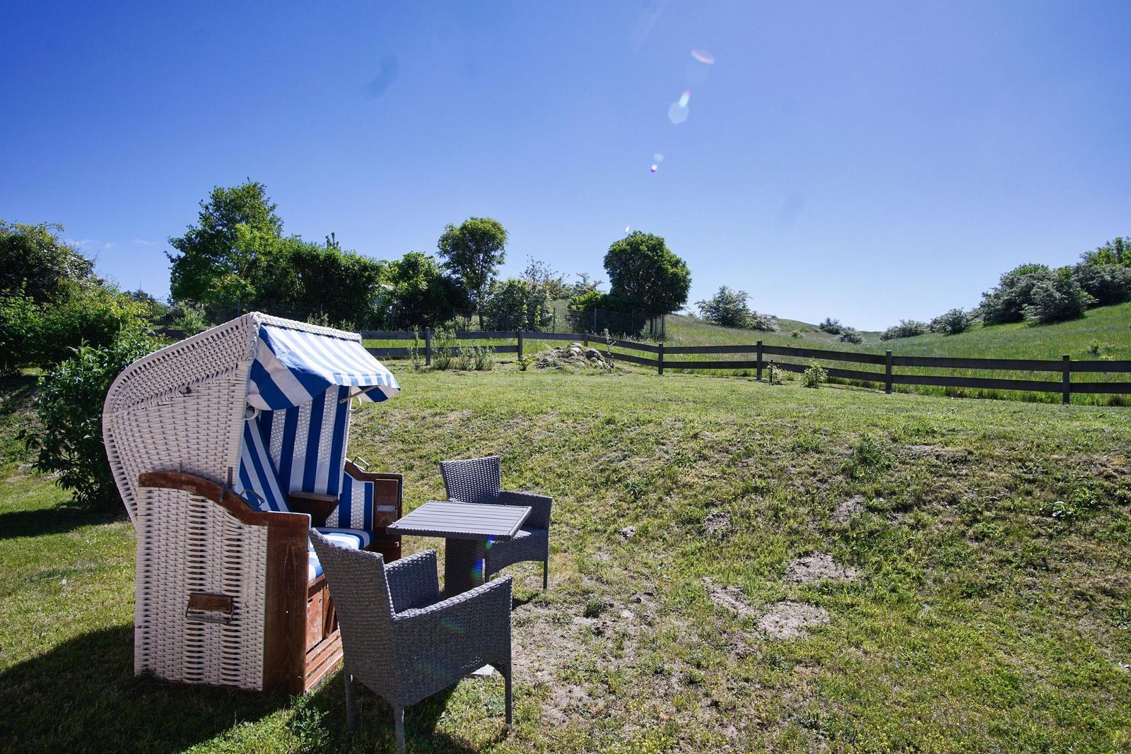 Wilde Strandkörbe und Tische im Garten mit Blick auf grüne Wiesen und Bäume.