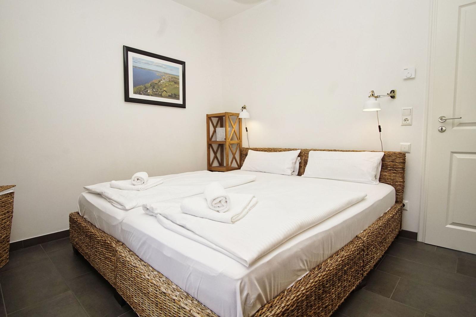 Schlafzimmer mit Bett aus geflochtenem Material, weiße Bettwäsche und Wandbild.
