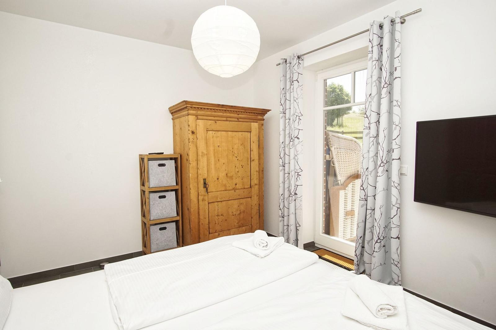 Schlafzimmer mit Bett, Holzschrank, Fenster und TV.