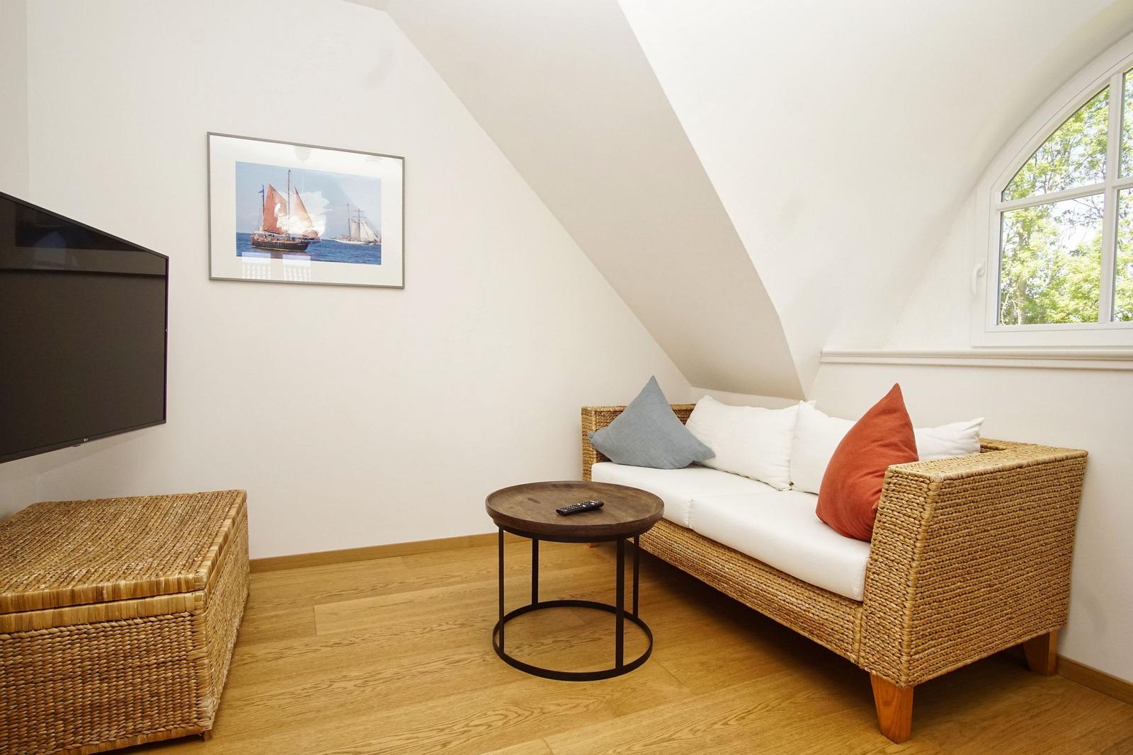 Wohnzimmer mit Sofa, Fernseher und Fenster. Holzboden und schräge Decke.