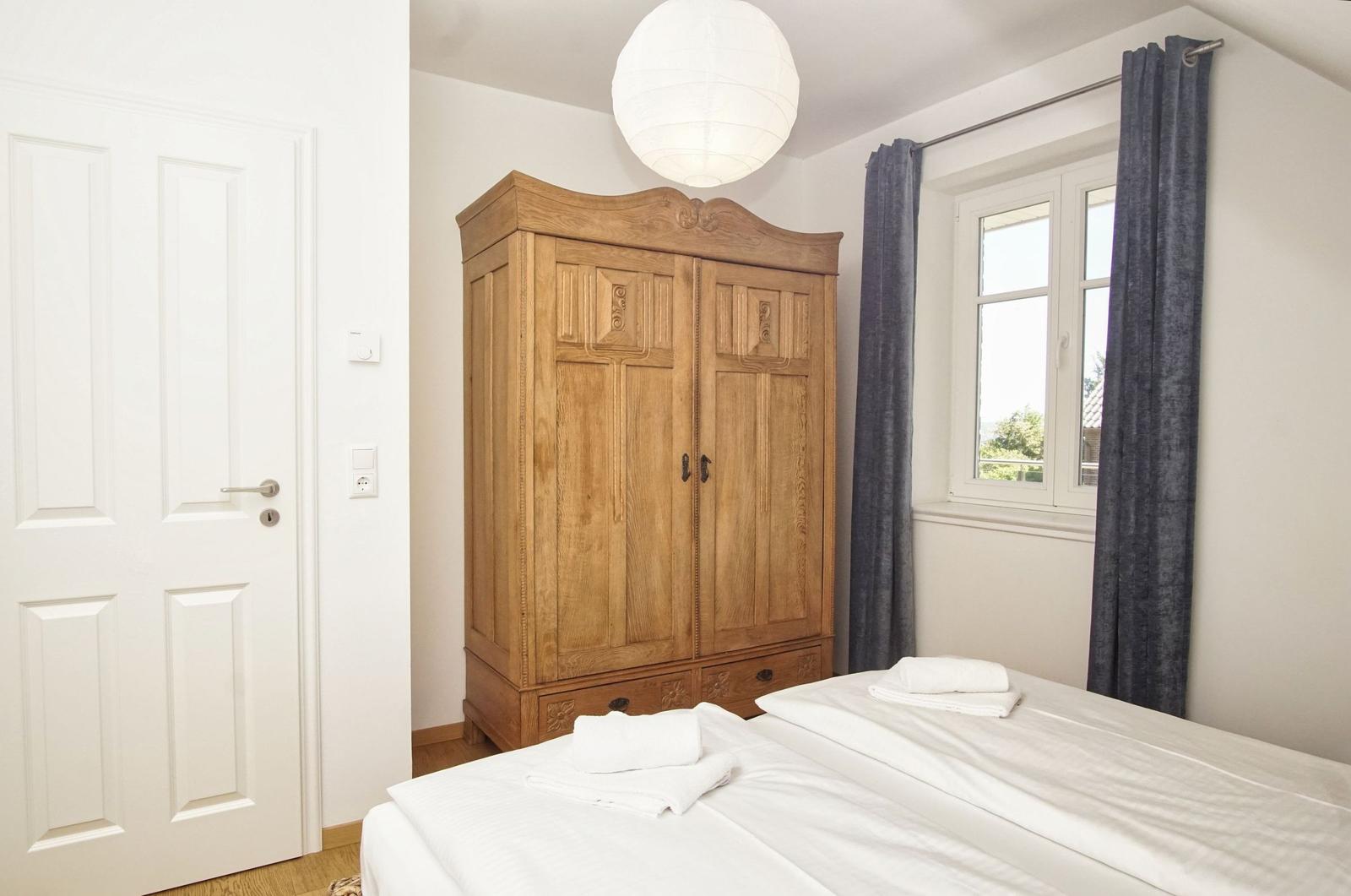 Schlafzimmer mit Holzschrank, Bett und Fenster mit Vorhängen.