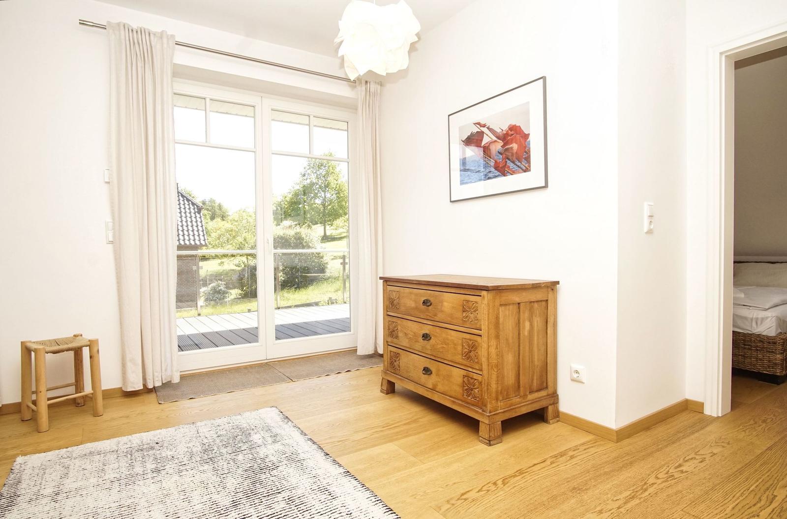 Ein Zimmer mit Holzboden, einem Schrank und einer Glastür zum Balkon.