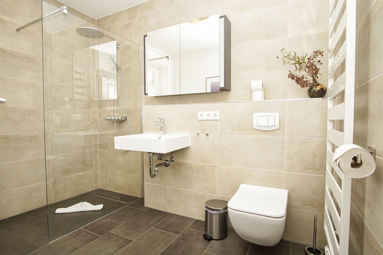 Moderne Badewanne mit Dusche, Waschbecken und Toilette. Fliesen und Spiegel sichtbar.