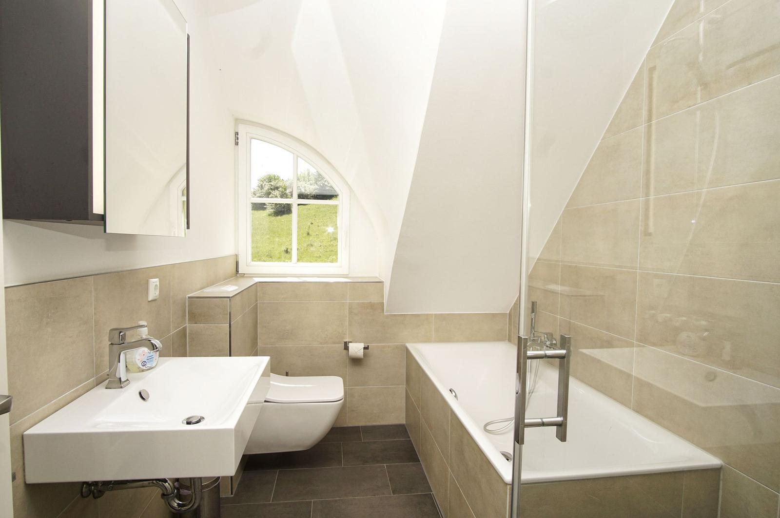 Badezimmer mit Badewanne, Toilette und Waschbecken unter einem Dachfenster.