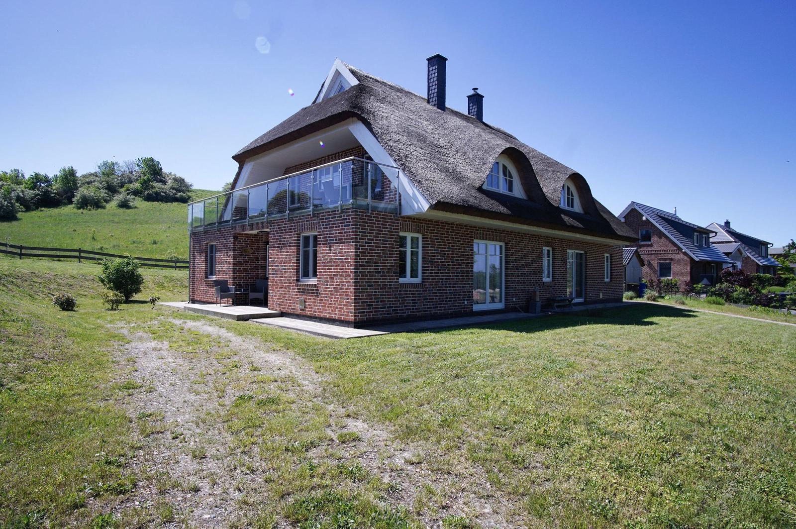 Ein zweistöckiges Haus mit Dachterrasse und Schornsteinen steht auf einer grünen Wiese.