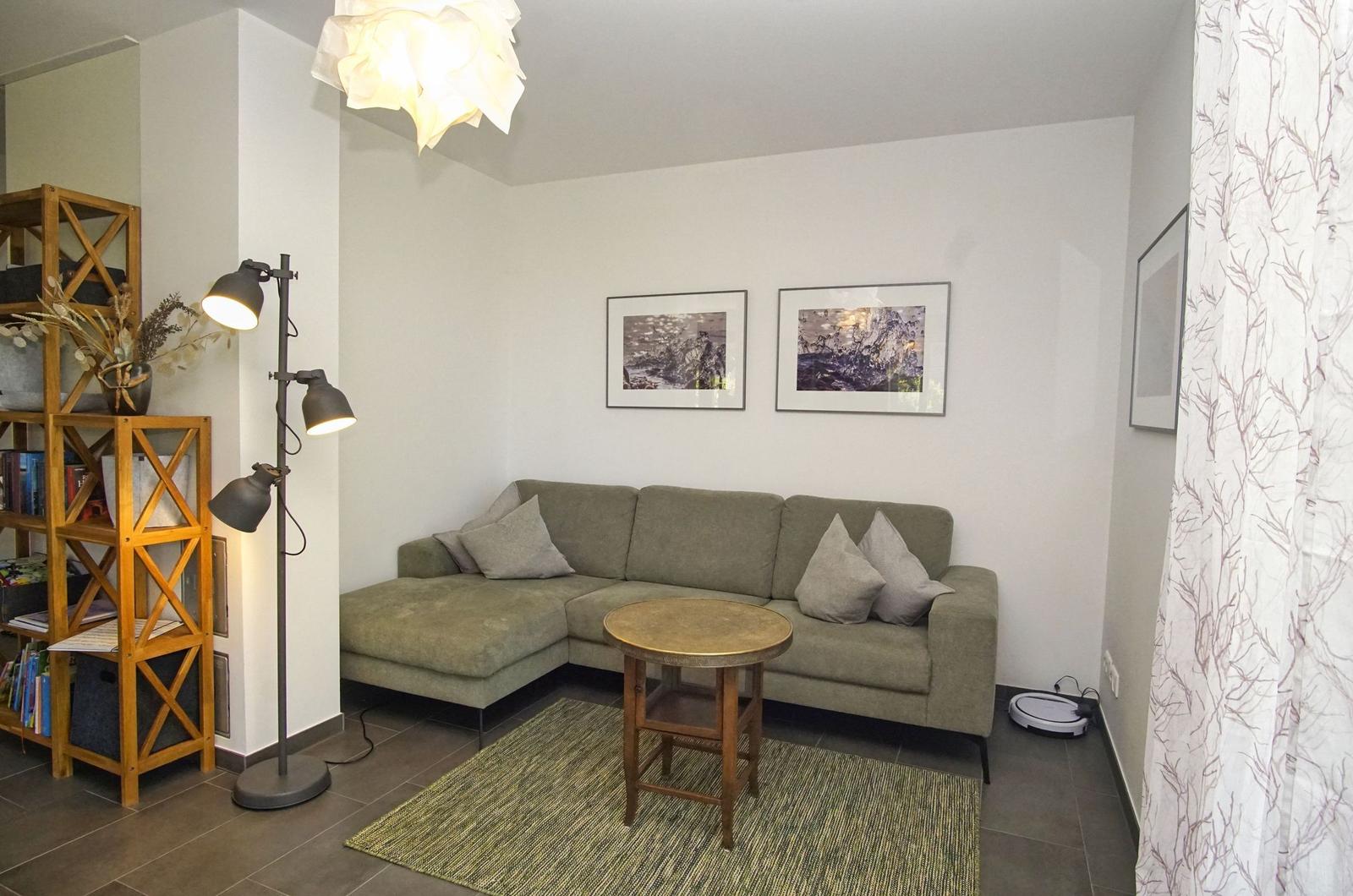 Wohnzimmer mit Ecksofa, Tisch, Stehlampe und Wandbildern.