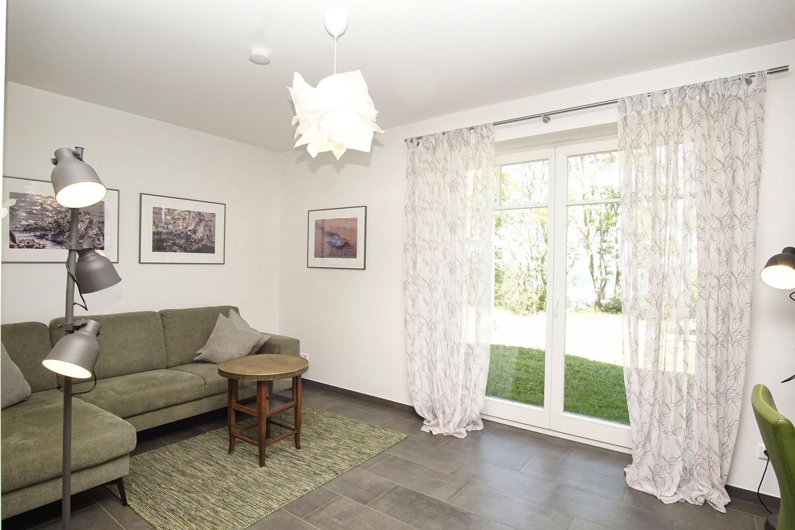 Wohnzimmer mit Sofa, Tisch und Fenster zur Grünfläche.