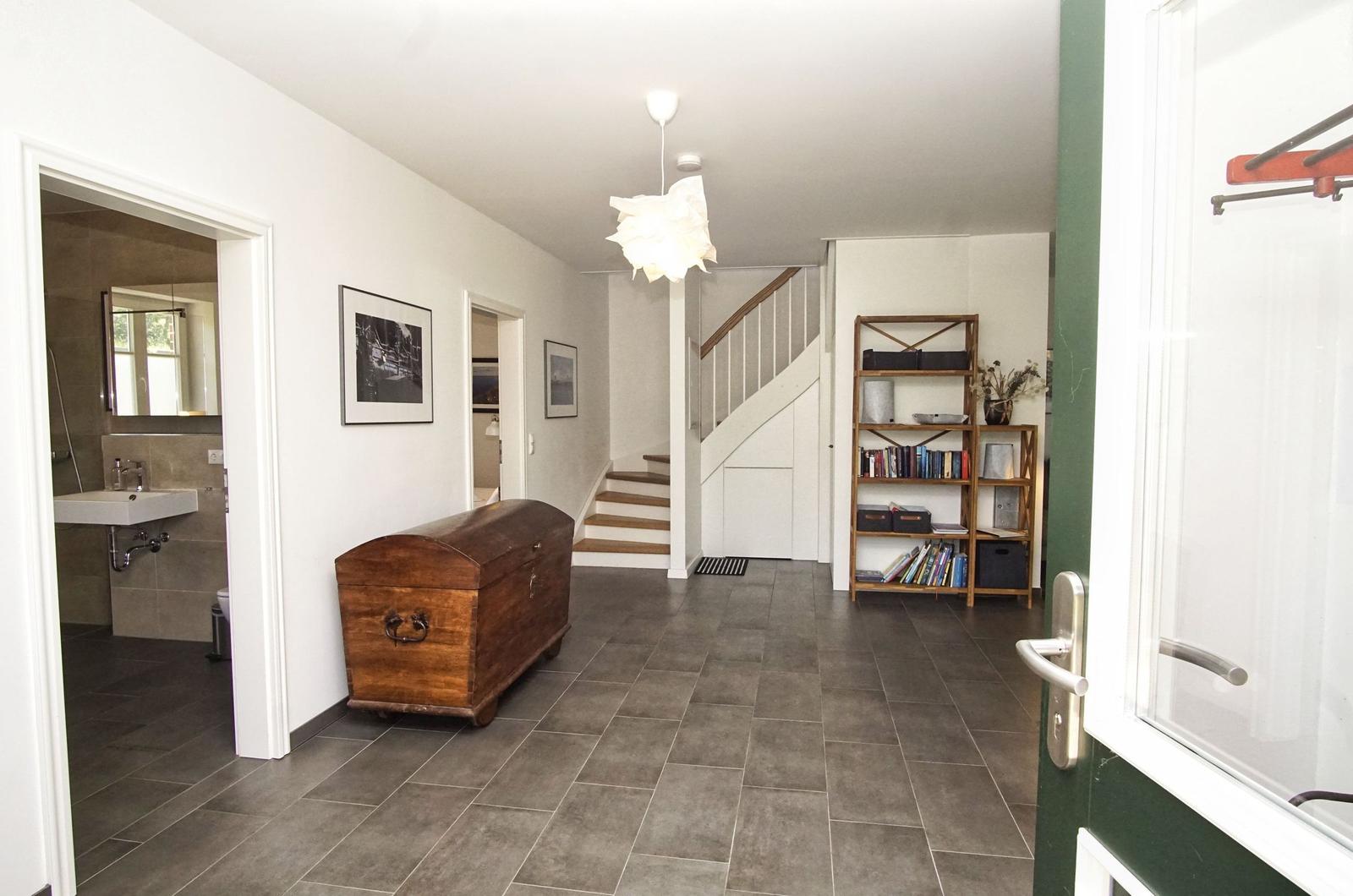 Haus mit Eingangsbereich, Treppenhaus und Bücherregal. Links Badezimmer, rechts Tür.