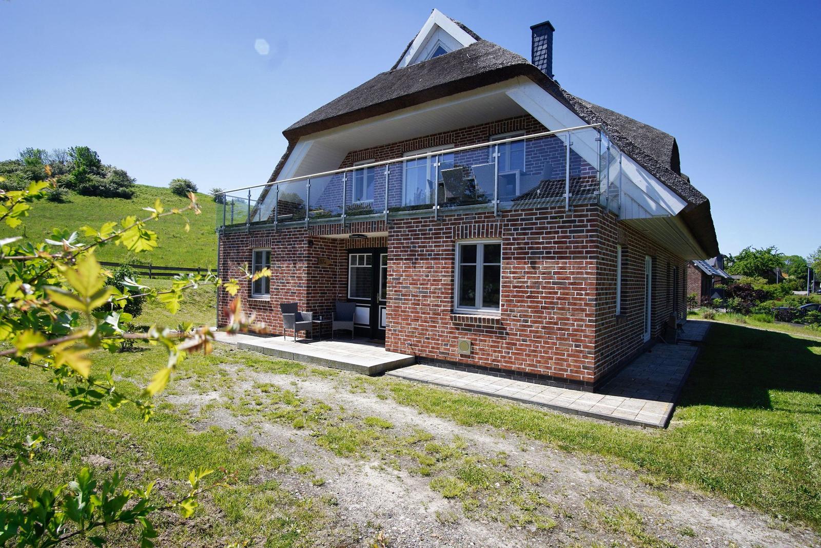 Ein zweistöckiges Haus mit Dachterrasse und Garten. Die Fassade ist aus rotem Backstein.