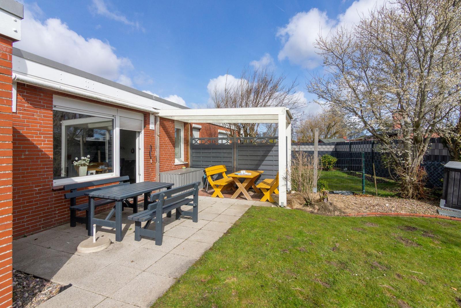 Hinterhof mit Terrasse, Tisch, Bänken und gelben Stühlen unter Pavillon.