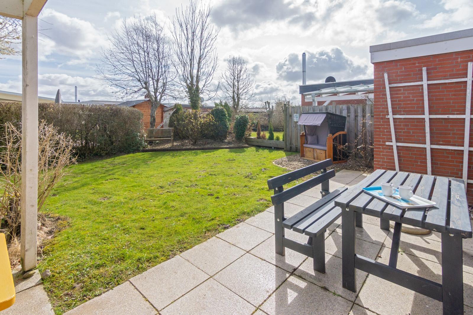 Hinterhof mit grünem Rasen, Terrasse und Holztisch mit Bänken.