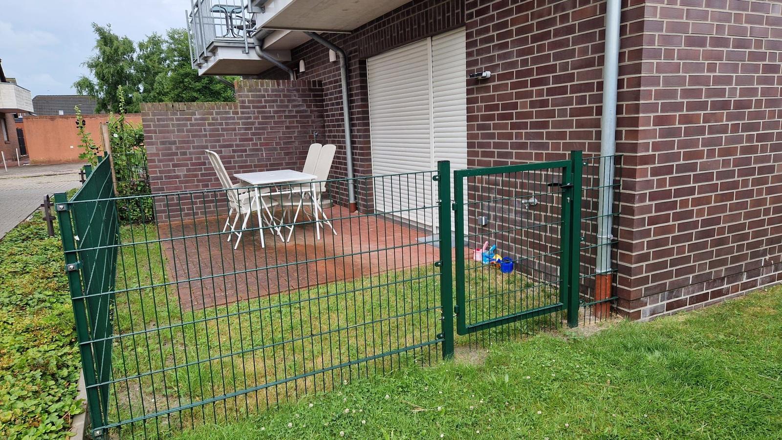 Hinterhof mit grünem Zaun, Terrasse und weißem Tisch mit Stühlen.