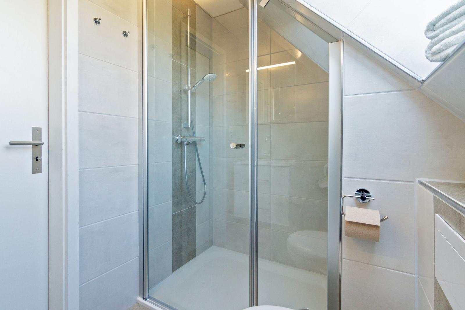 Dusche mit Glaswand, Toilette und Toilettenpapierhalter in einem Badezimmer mit Dachschrägen.