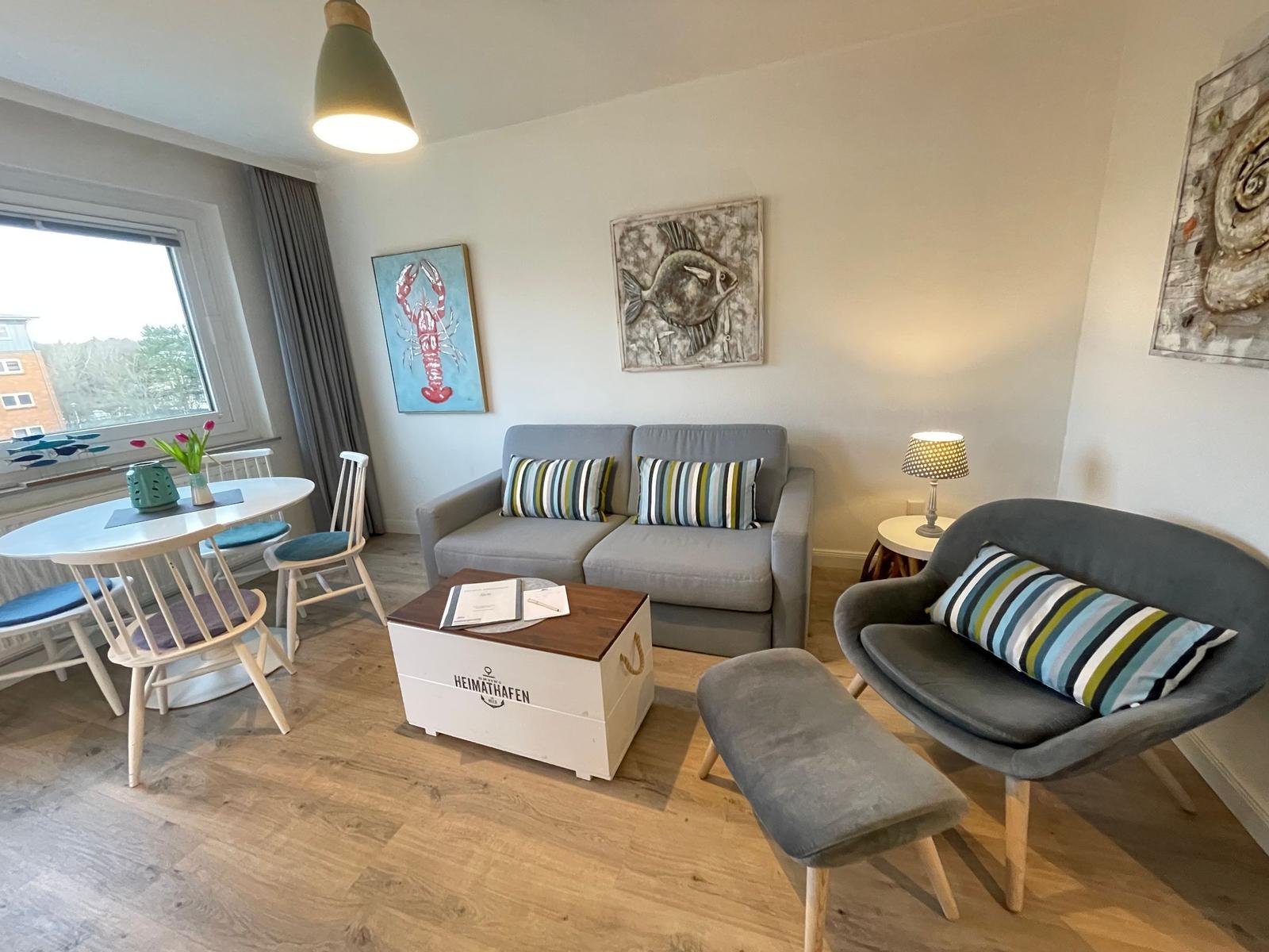 Wohnzimmer mit Sofa, Sessel und Esstisch. Wandbilder zeigen Fisch und Hummer.