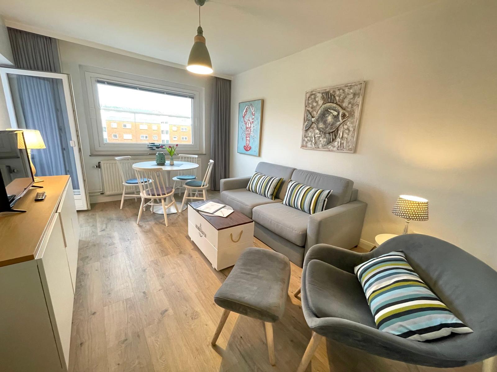 Wohnzimmer mit Sofa, Sessel, Esstisch und Fenster. Wanddekoration mit Fisch- und Hummerbildern.