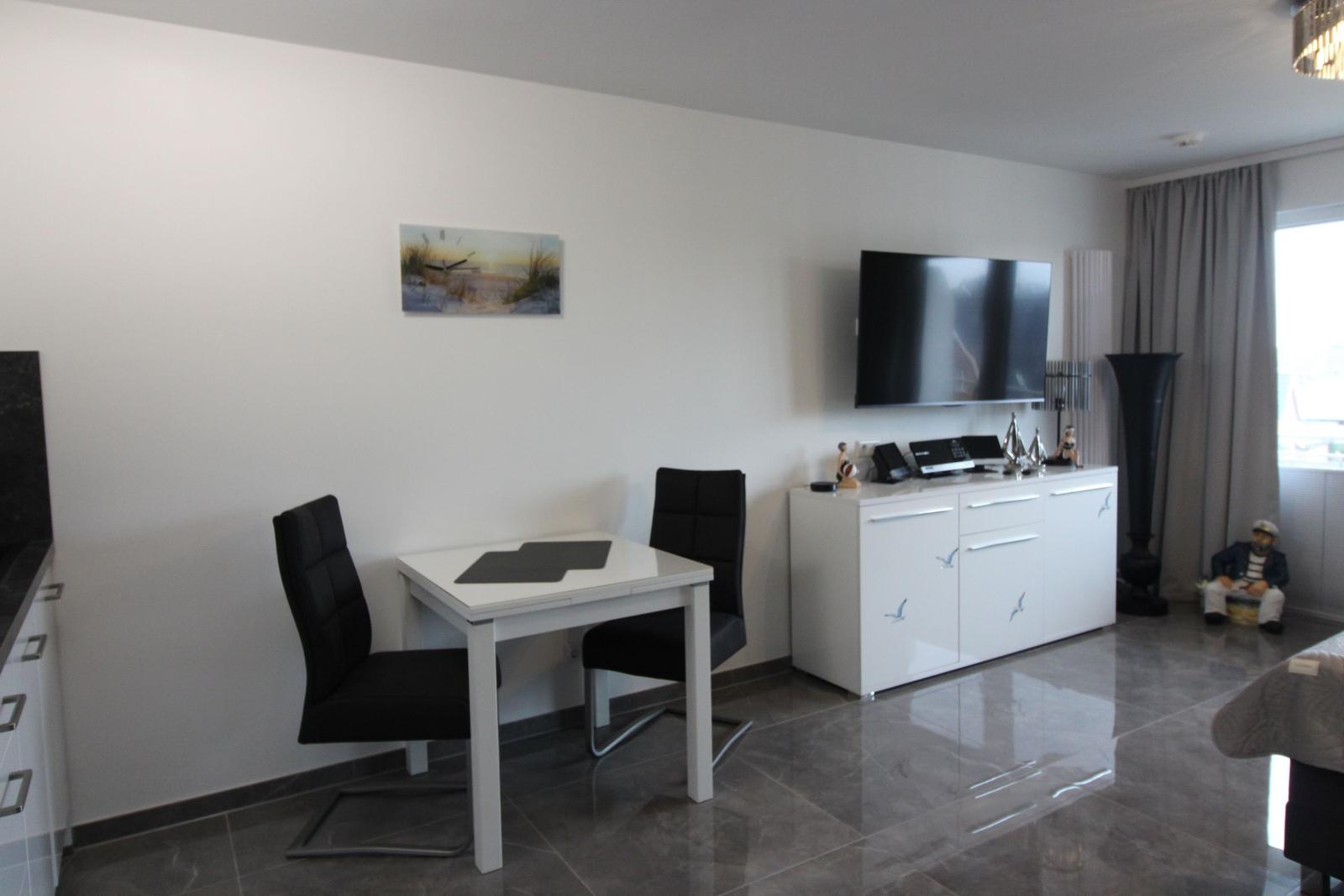 Ein Essbereich mit Tisch und zwei Stühlen neben einem weißen Sideboard mit Fernseher.