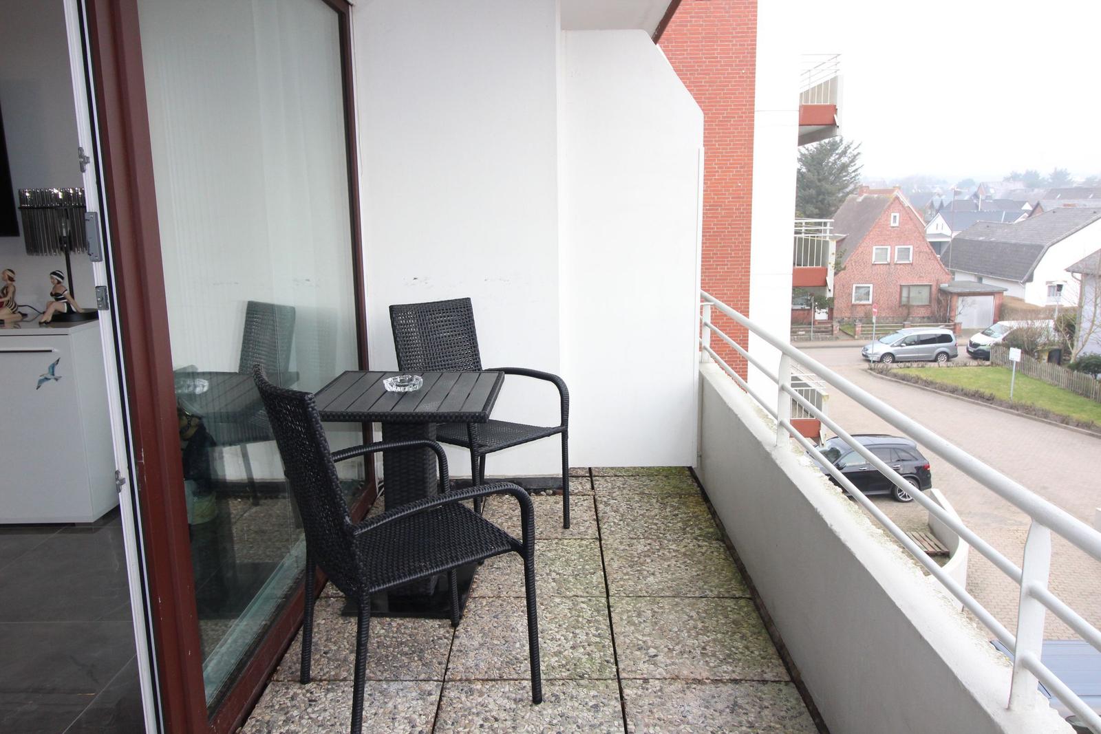 Balkon mit Tisch und zwei Stühlen, Blick auf Straße und Häuser.