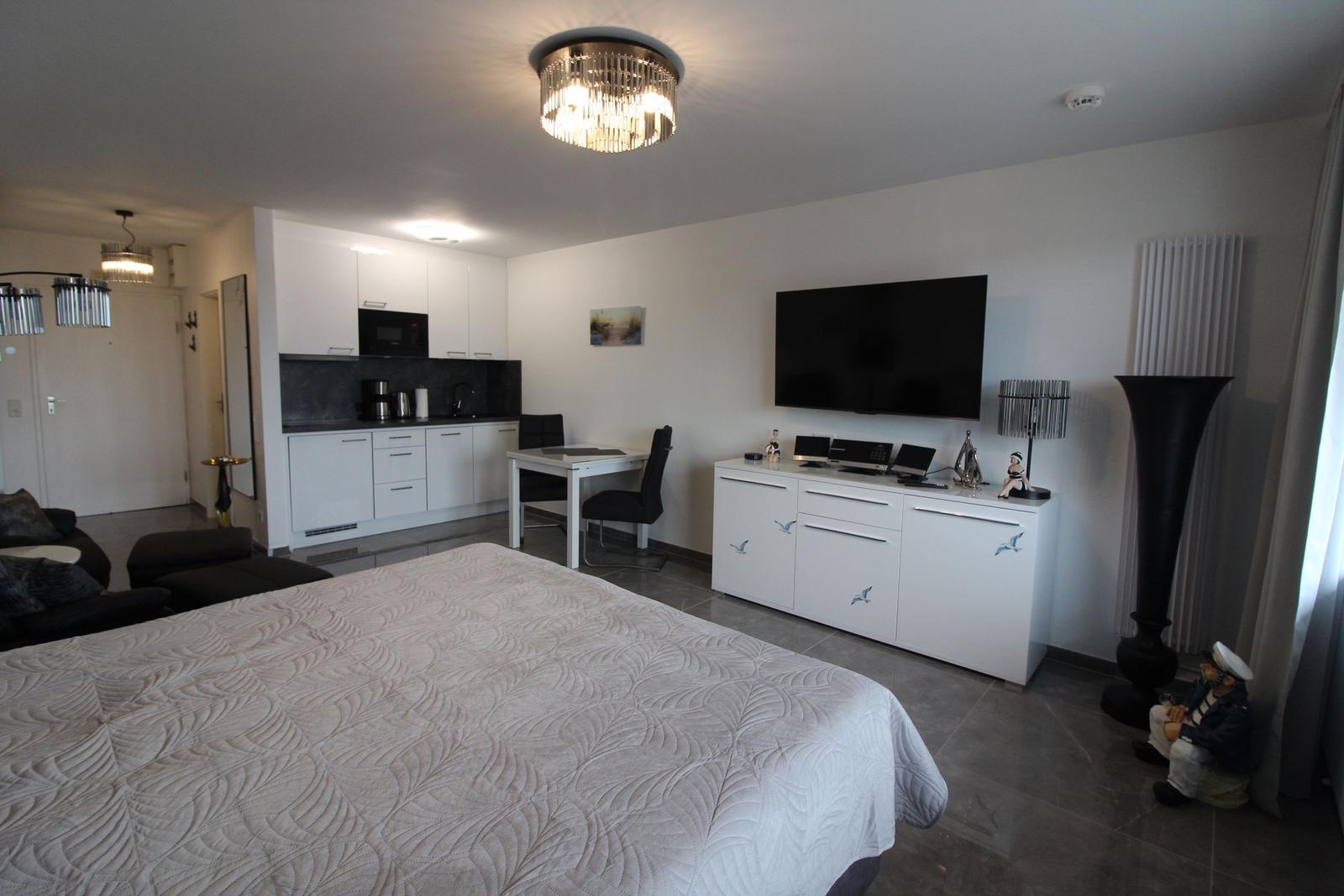 Schlafzimmer mit Küchenbereich und Fernseher. Modern eingerichtet mit weißen Möbeln.