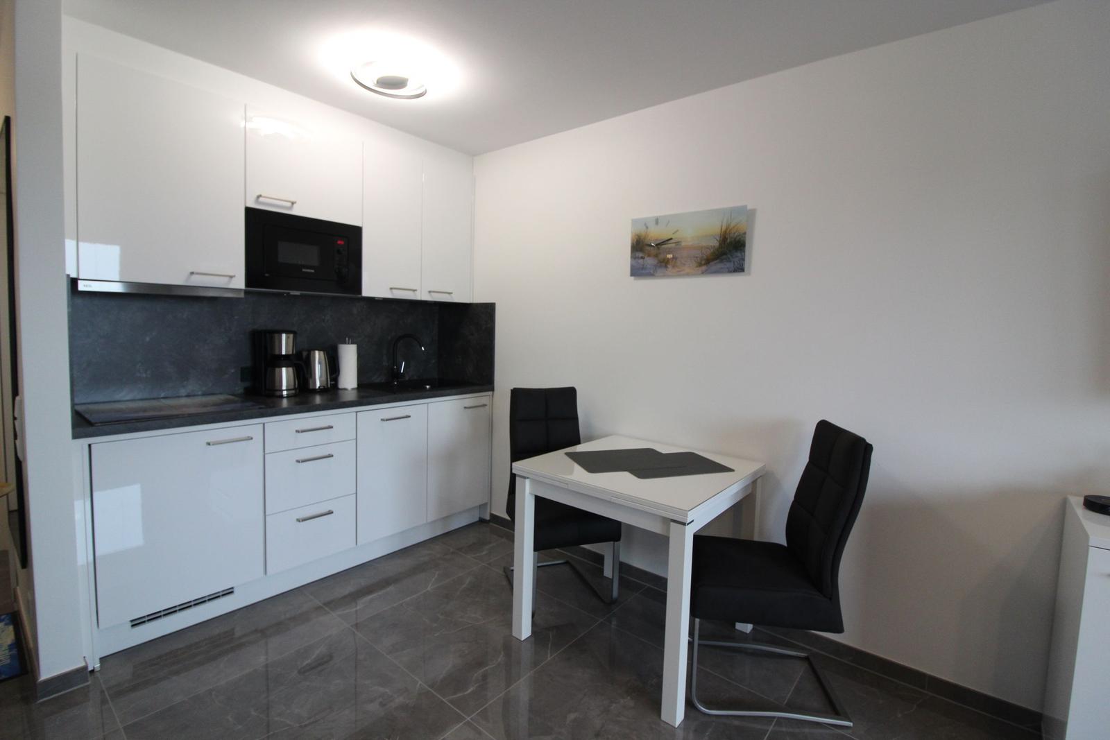 Küche mit Essbereich, weißer Arbeitsplatte, schwarzen Stühlen und Wandbild.