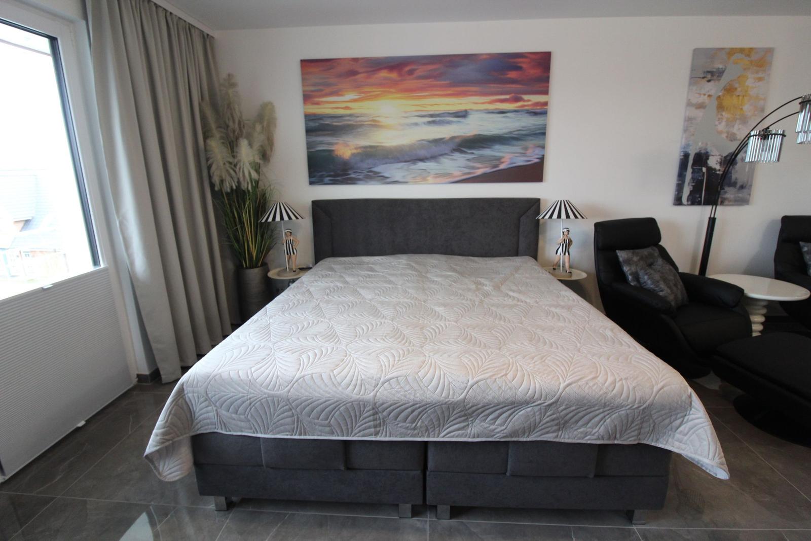 Schlafzimmer mit großem Bett, Wandbild und Sitzgelegenheiten.