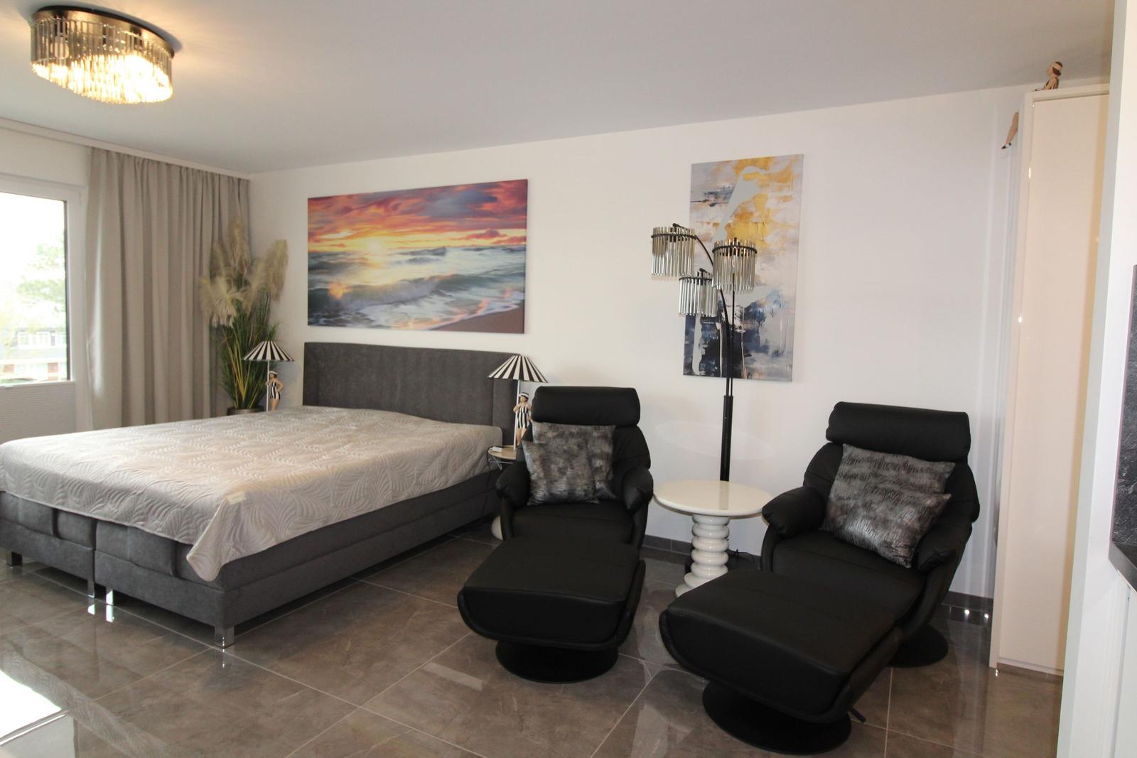 Schlafzimmer mit Bett, zwei Sesseln und Wandbildern.