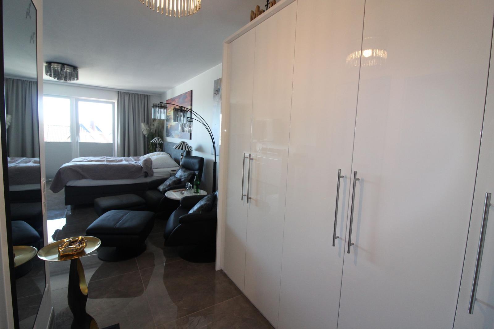 Schlafzimmer mit weißen Schränken, schwarzer Couch und großem Fenster.