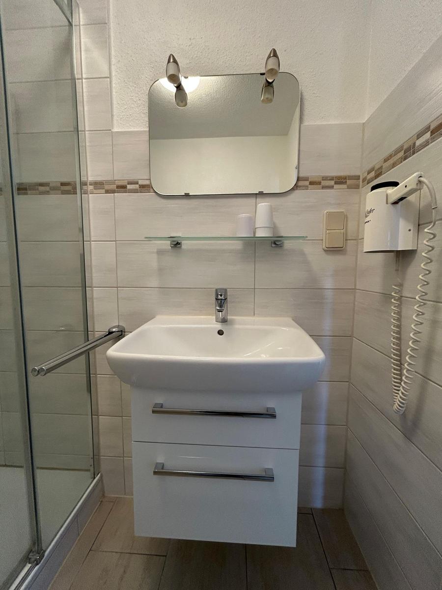 Badezimmer mit Dusche, Waschbecken und Spiegel