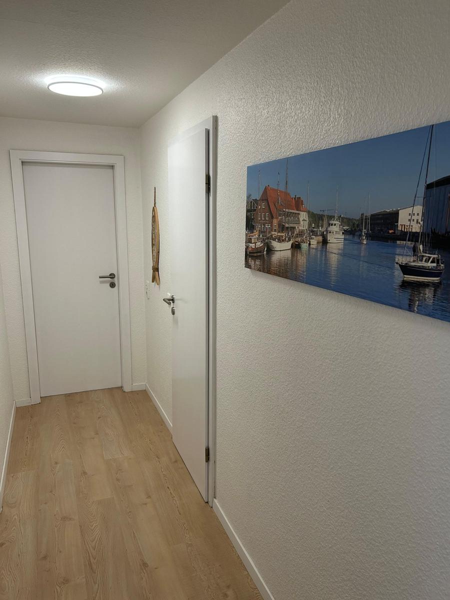 Flur mit Holzboden, zwei Türen und Wandbild mit Hafenansicht.