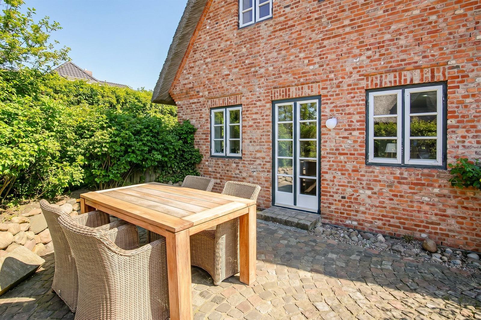 Backyard with wooden table and chairs in front of brick house with glass door.
