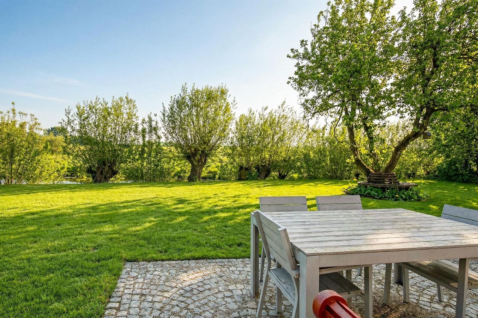 Hinterhof mit Tisch und Stühlen auf Kiesfläche, umgeben von Gras und Bäumen.