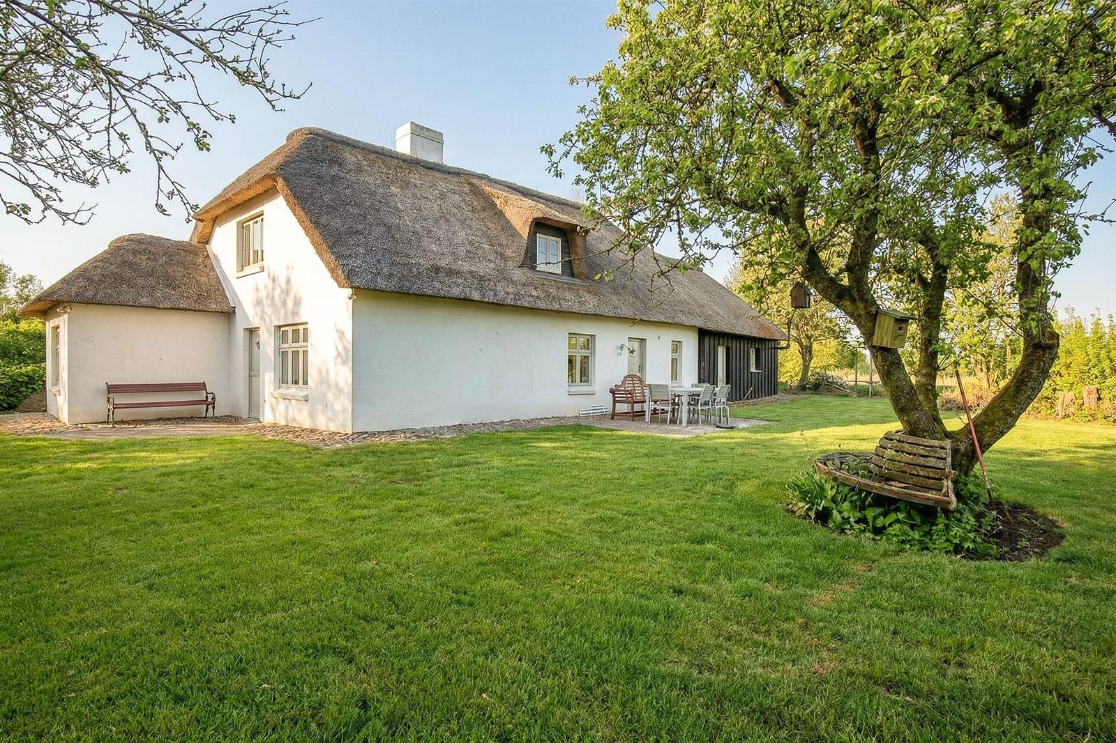 Ein Haus mit Strohdach, Garten und Bänken unter Bäumen.
