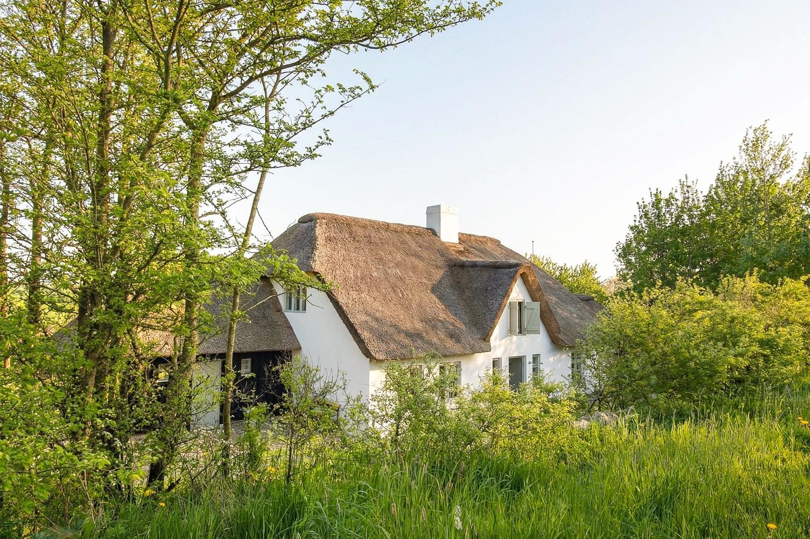 Haus mit Strohdach und weißen Wänden in grüner Umgebung.
