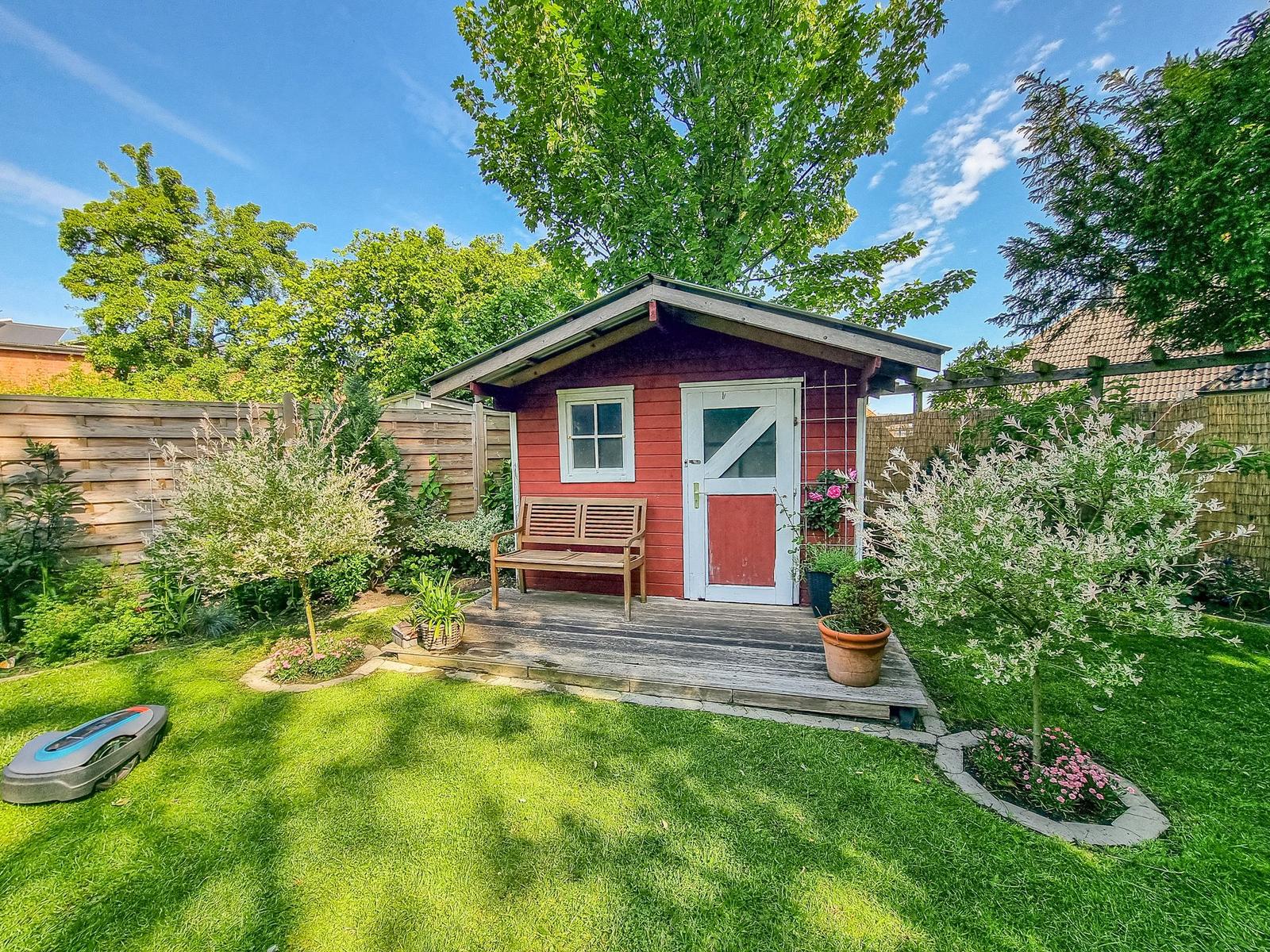 Rotes Holzhaus mit weißer Tür und Bank auf Terrasse im Garten.