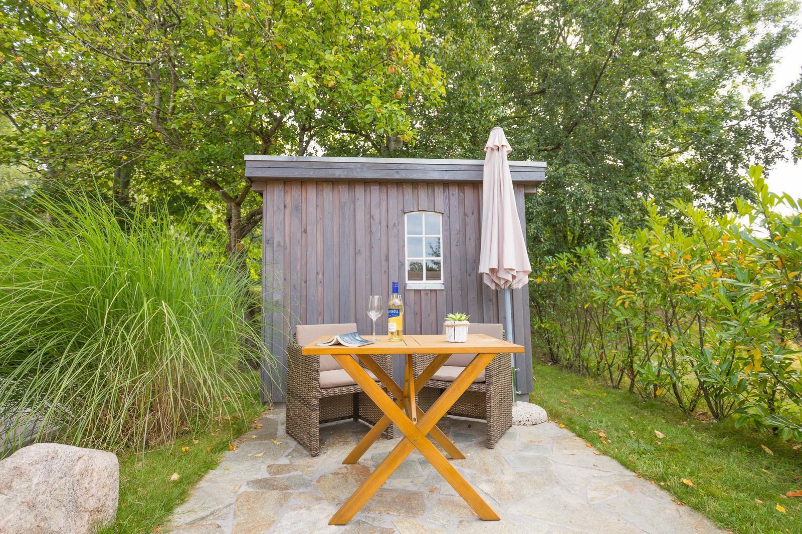 Wooden table with two chairs in front of a wooden shed in the garden.