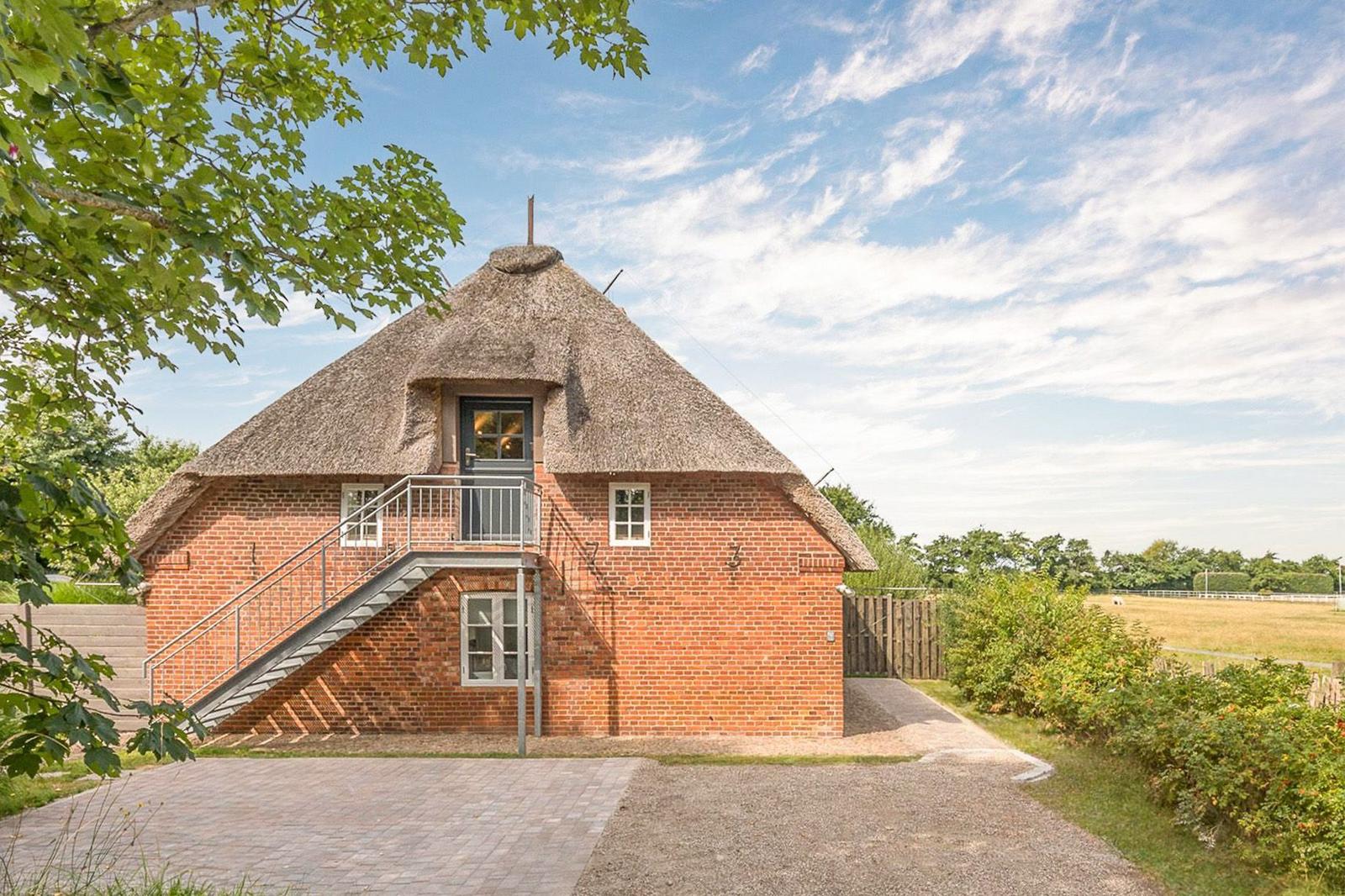 Red brick house with thatched roof and metal stairs to the entrance door.