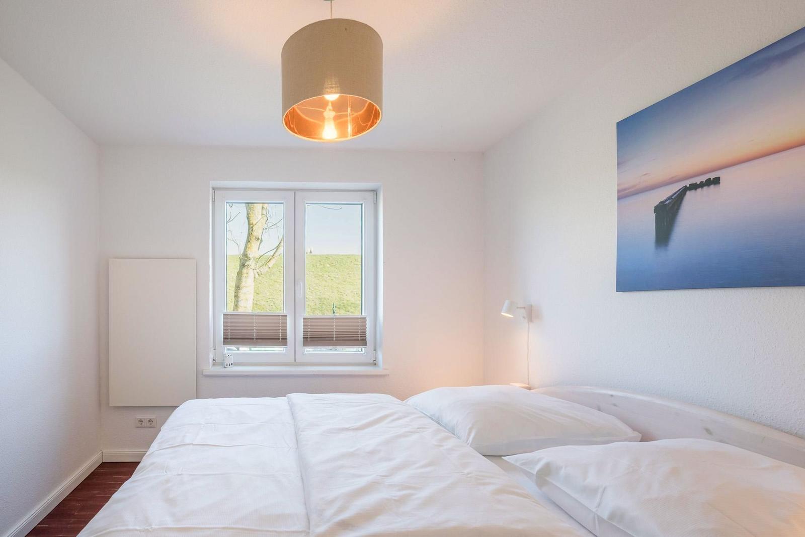 Schlafzimmer mit Doppelbett, Fenster mit Blick auf Grünfläche und Wandbild mit Hafen.
