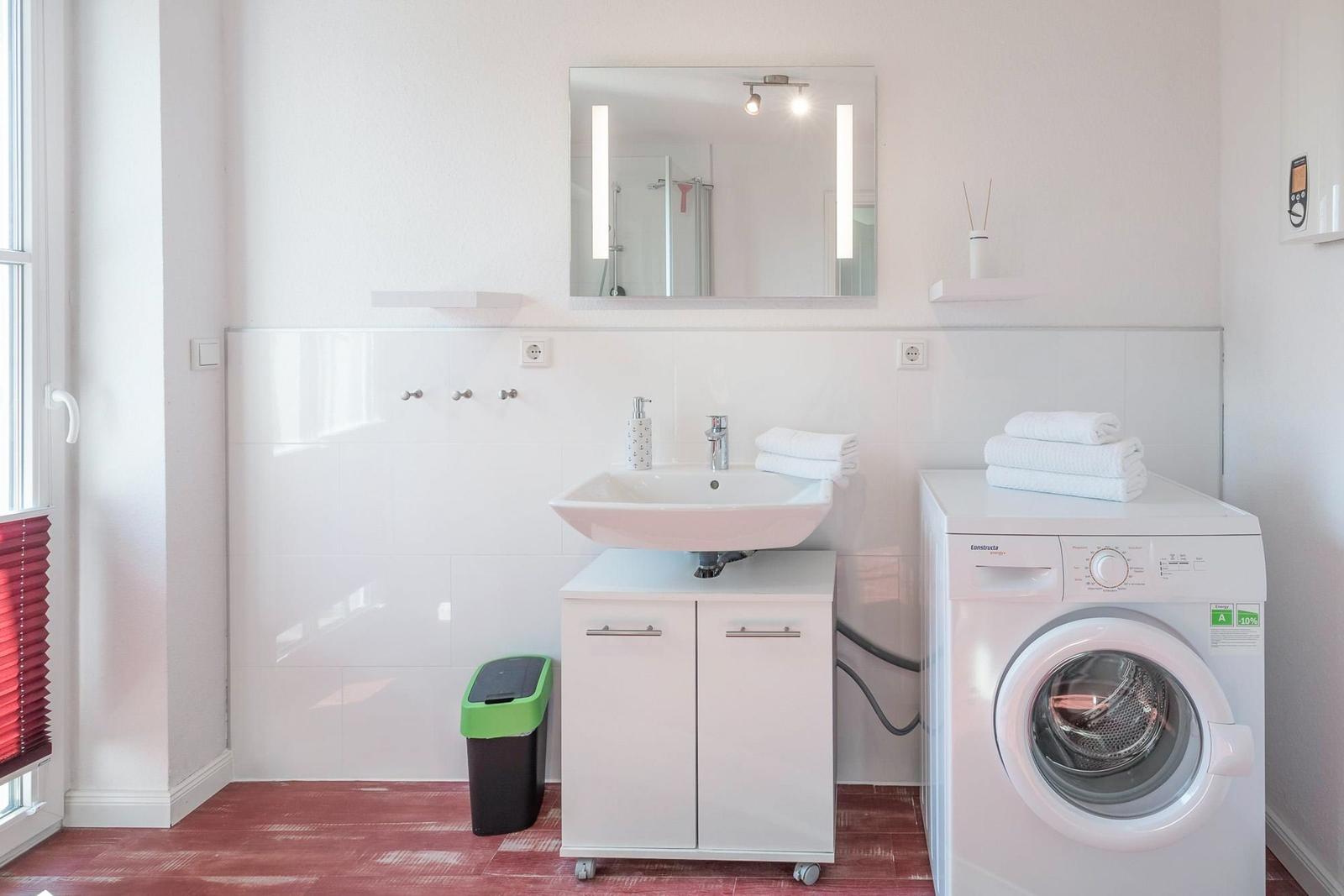 Badezimmer mit Waschmaschine, Spiegel und Waschbecken. Fliesenwand und roter Boden.