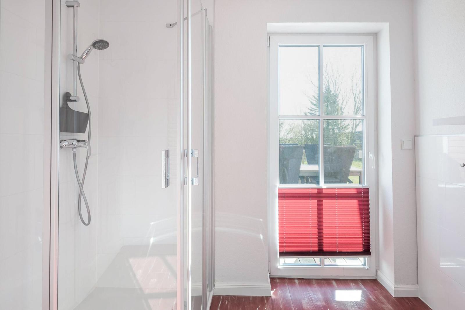 Dusche mit Glaswand und Fenster mit roten Jalousien.