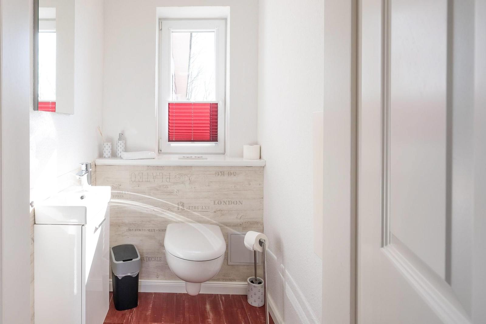 Badezimmer mit Toilette, Waschbecken und Fenster mit roten Jalousien.