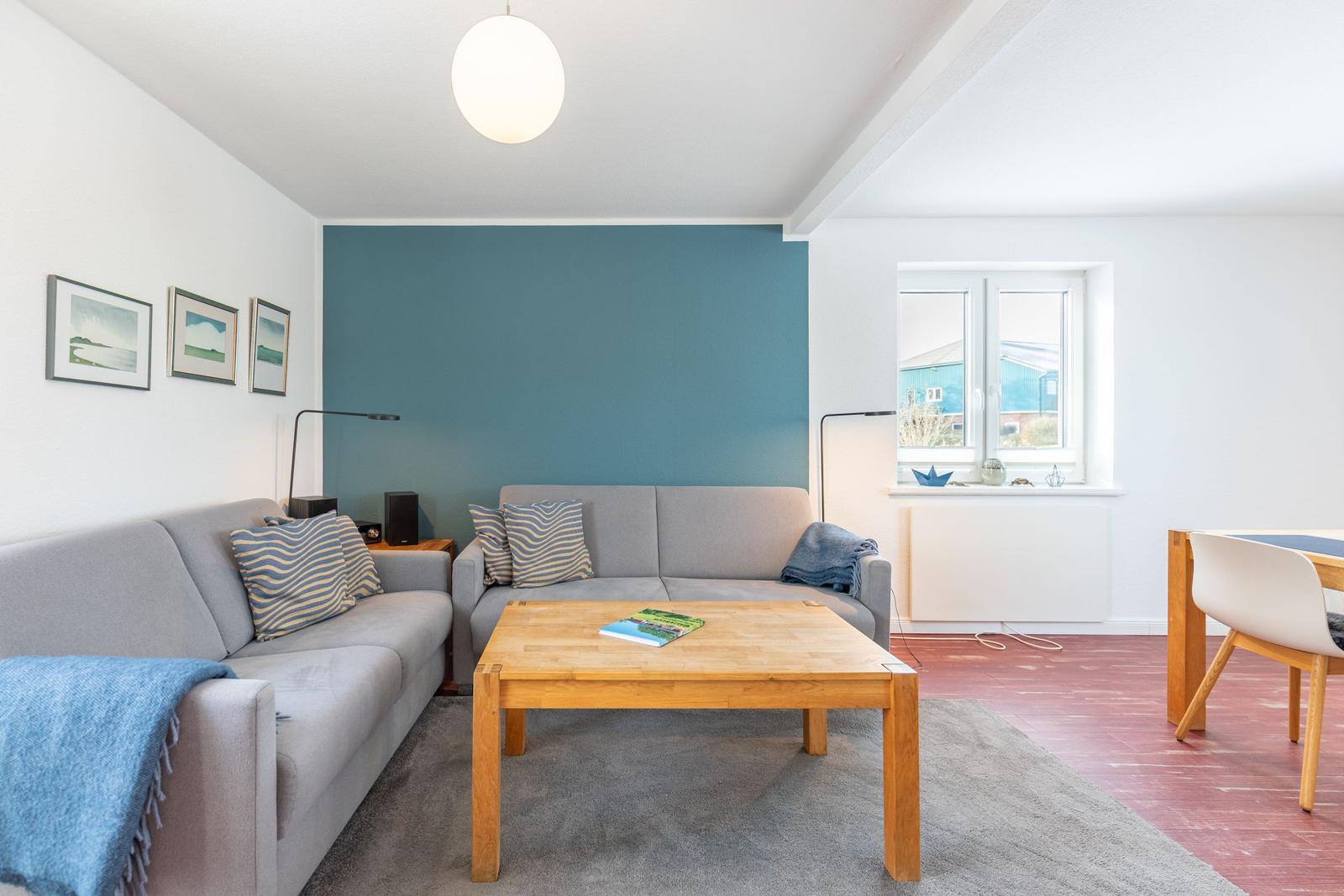 Wohnzimmer mit Sofa, Tisch und Fenster. Wand in Blau. Teppich und Holzboden.