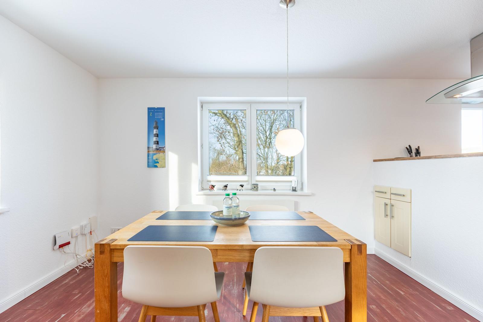 Esszimmer mit Holztisch, Stühlen und Fensterblick auf Bäume.