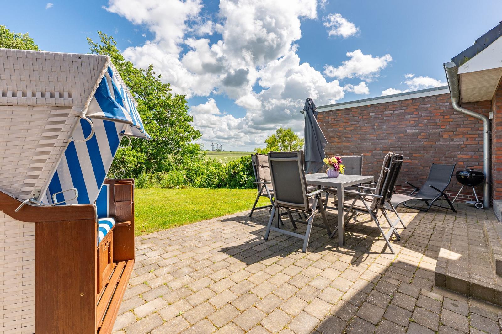 Terrasse mit Liege, Tisch, Stühlen und Grill. Blick auf Grünland und Windkraftanlagen.