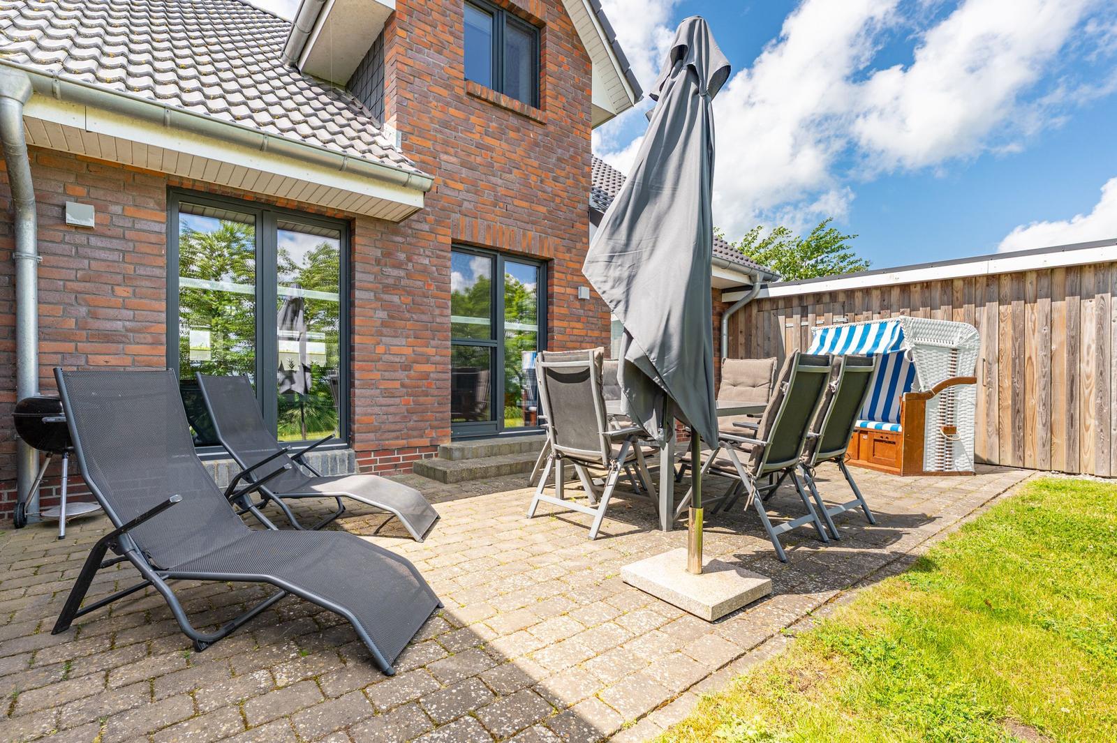 Terrasse mit Liegen, Tisch, Stühlen und Sonnenschirm neben einem Haus mit Backsteinfassade.