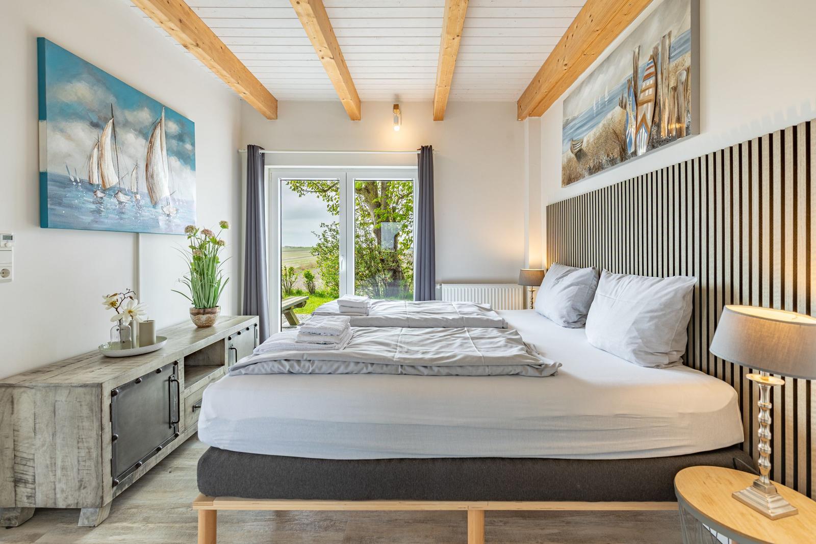 Schlafzimmer mit Doppelbett, Holzbalkendecke und Blick auf Grünflächen.